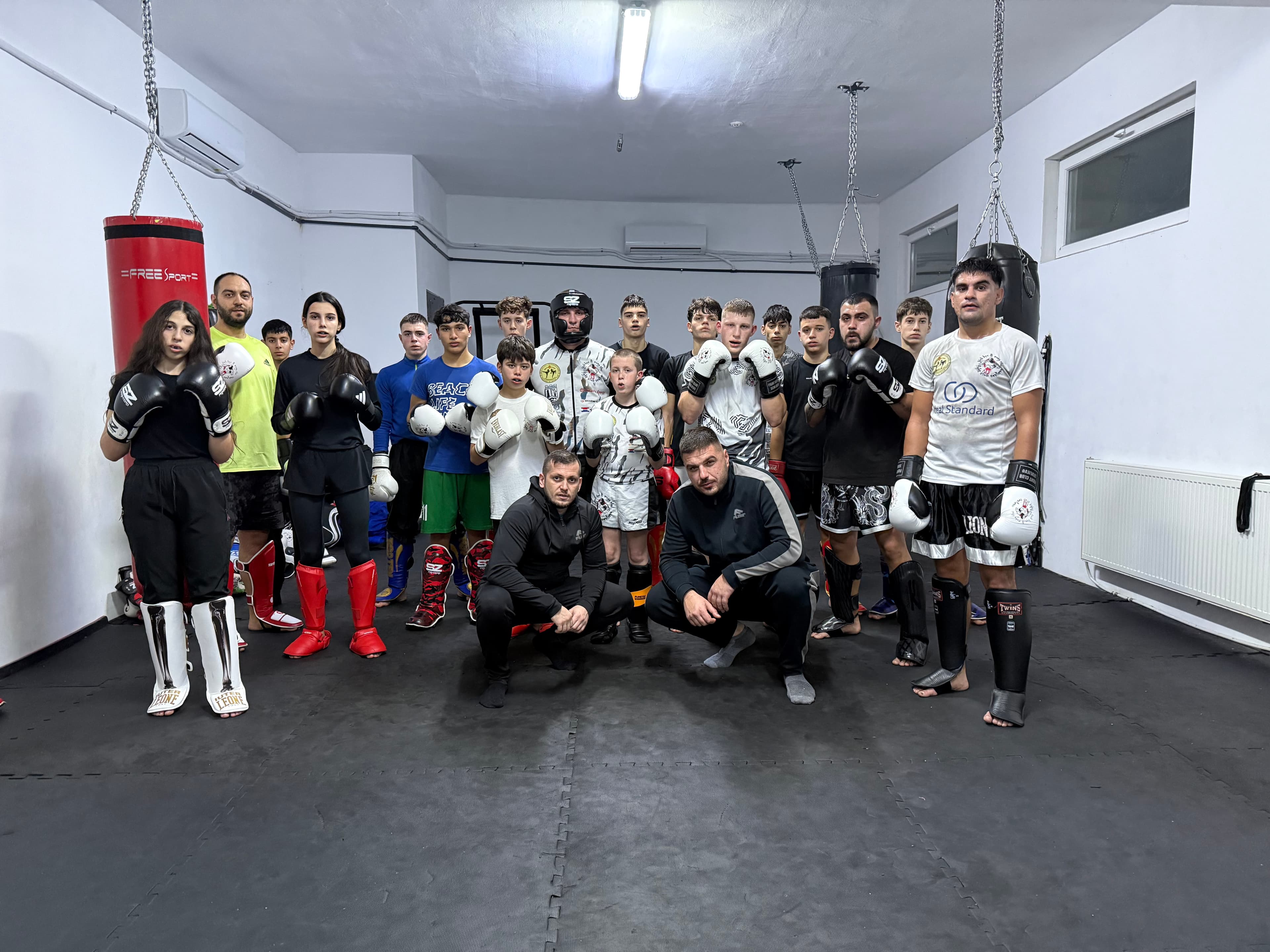 Diverse group of young kickboxers in training gear posing with two coaches in a gym.