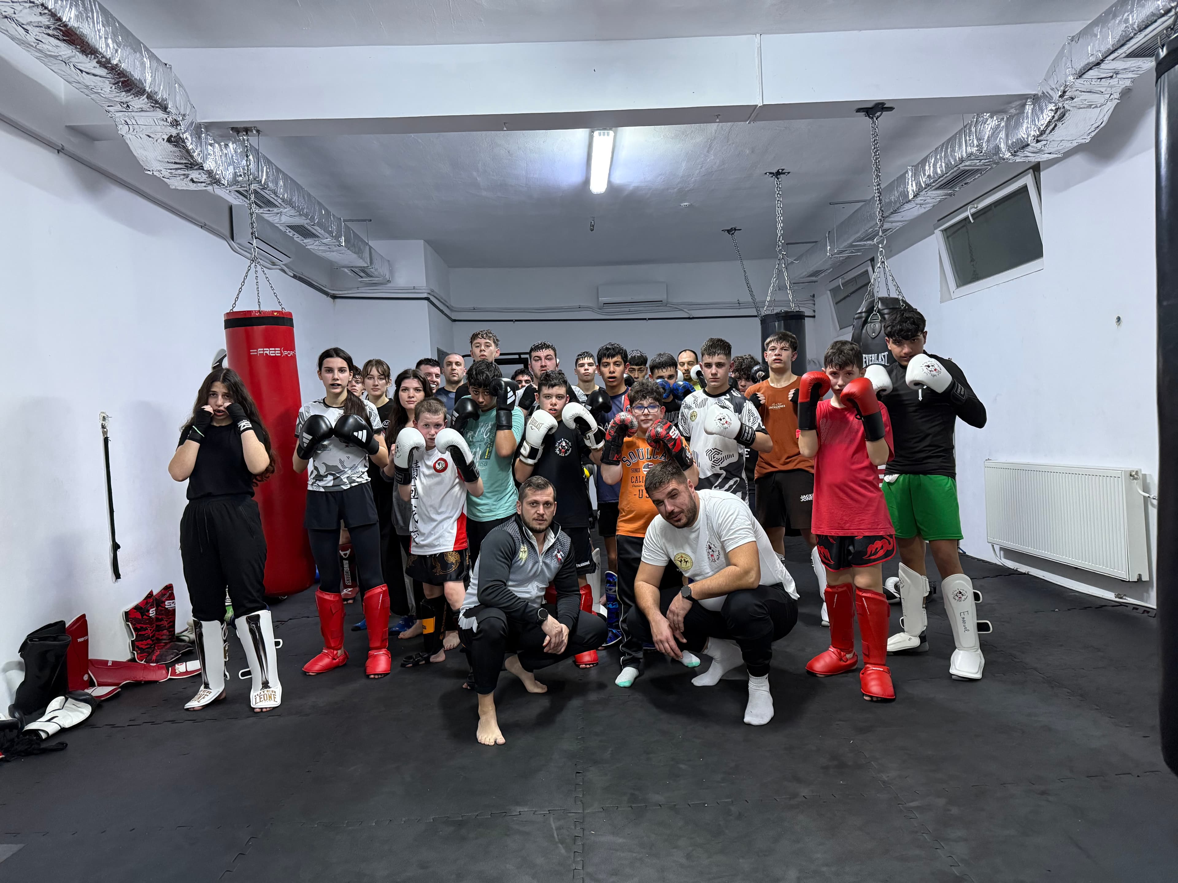 Youth kickboxing class and coaches posing in a gym with heavy punching bags.