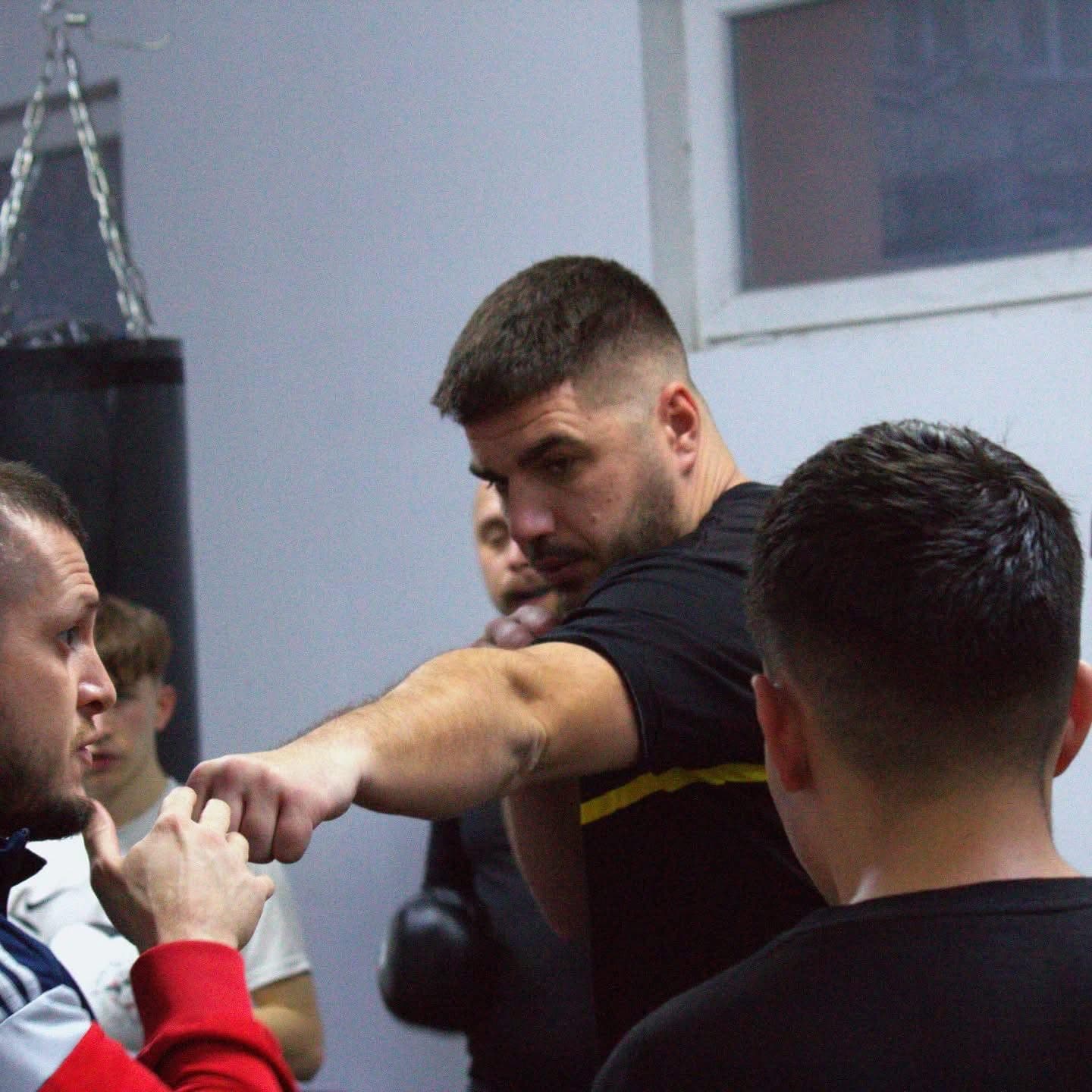 Boxing coach demonstrates a punch to a student during a training session in a gym.