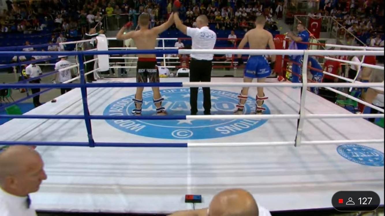 Referee raises the arm of a victorious kickboxer in a ring before a large crowd.