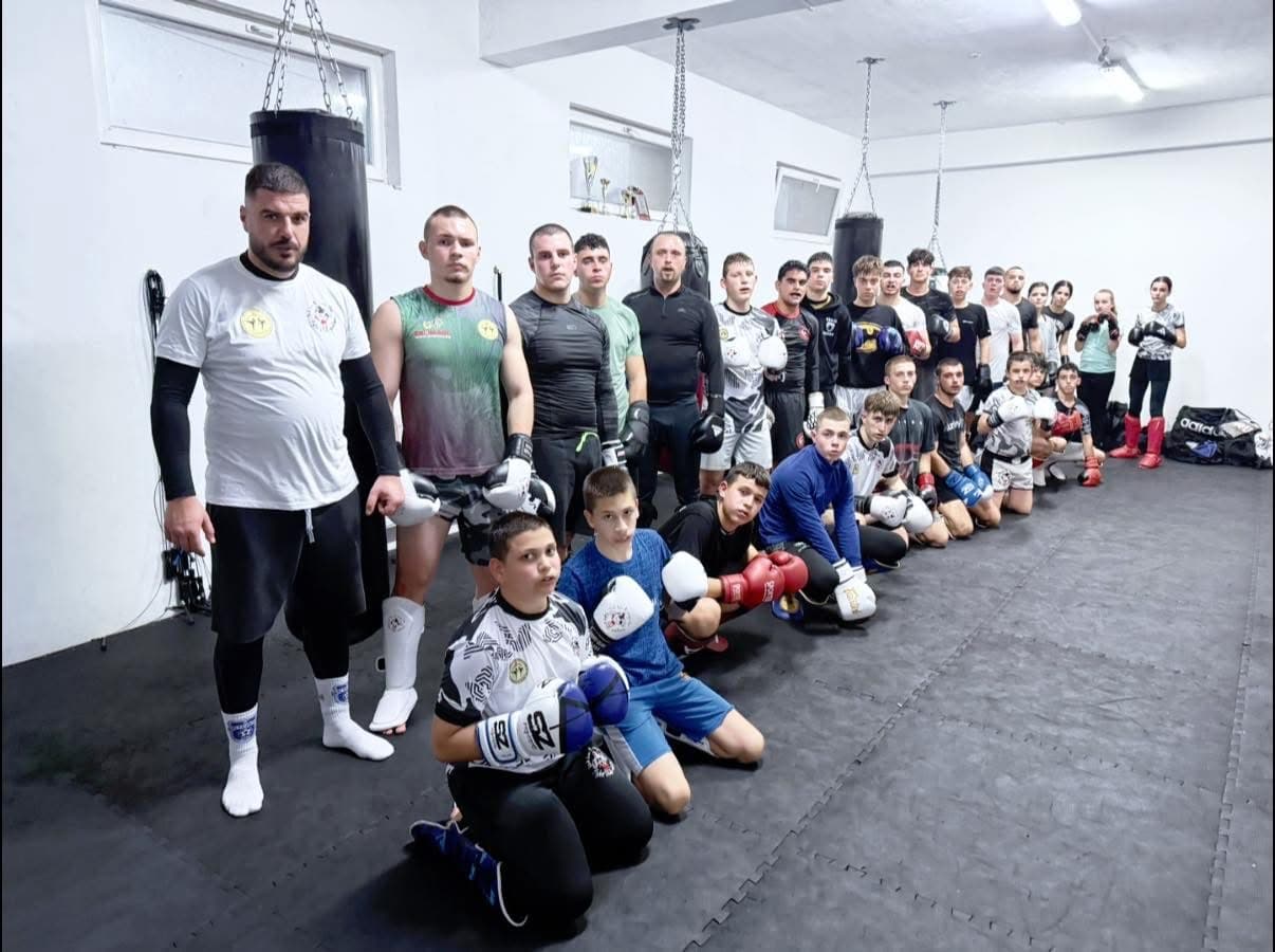 Martial arts students in boxing gear pose with their instructor in a training gym.